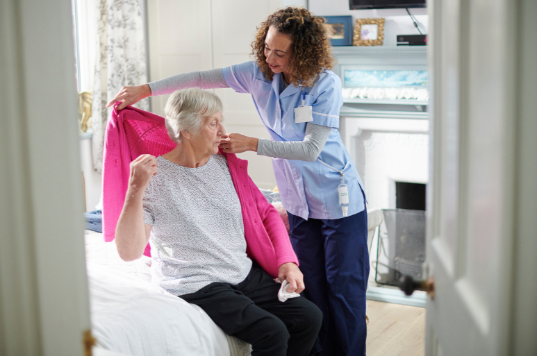Caregiver helping senior to wear a sweater - QAL Care Services